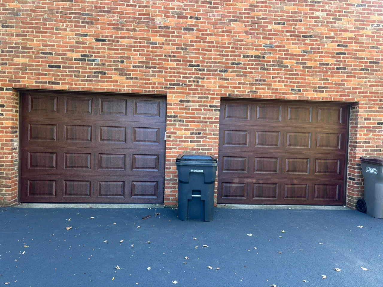 Two brown raised-panel garage doors in a brick building