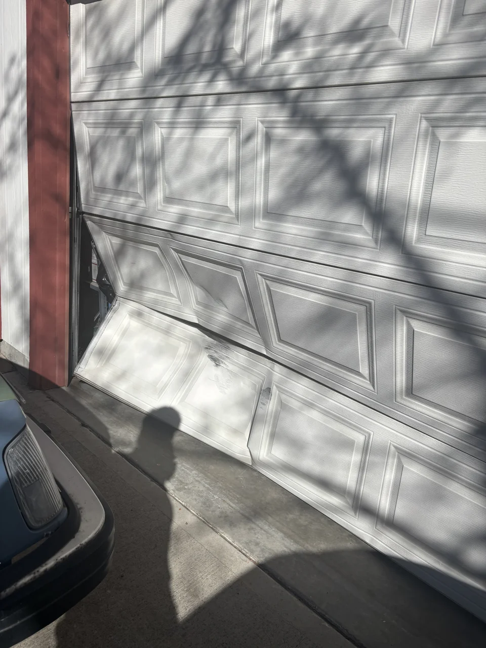 Damaged white garage door that is off track and needs repair